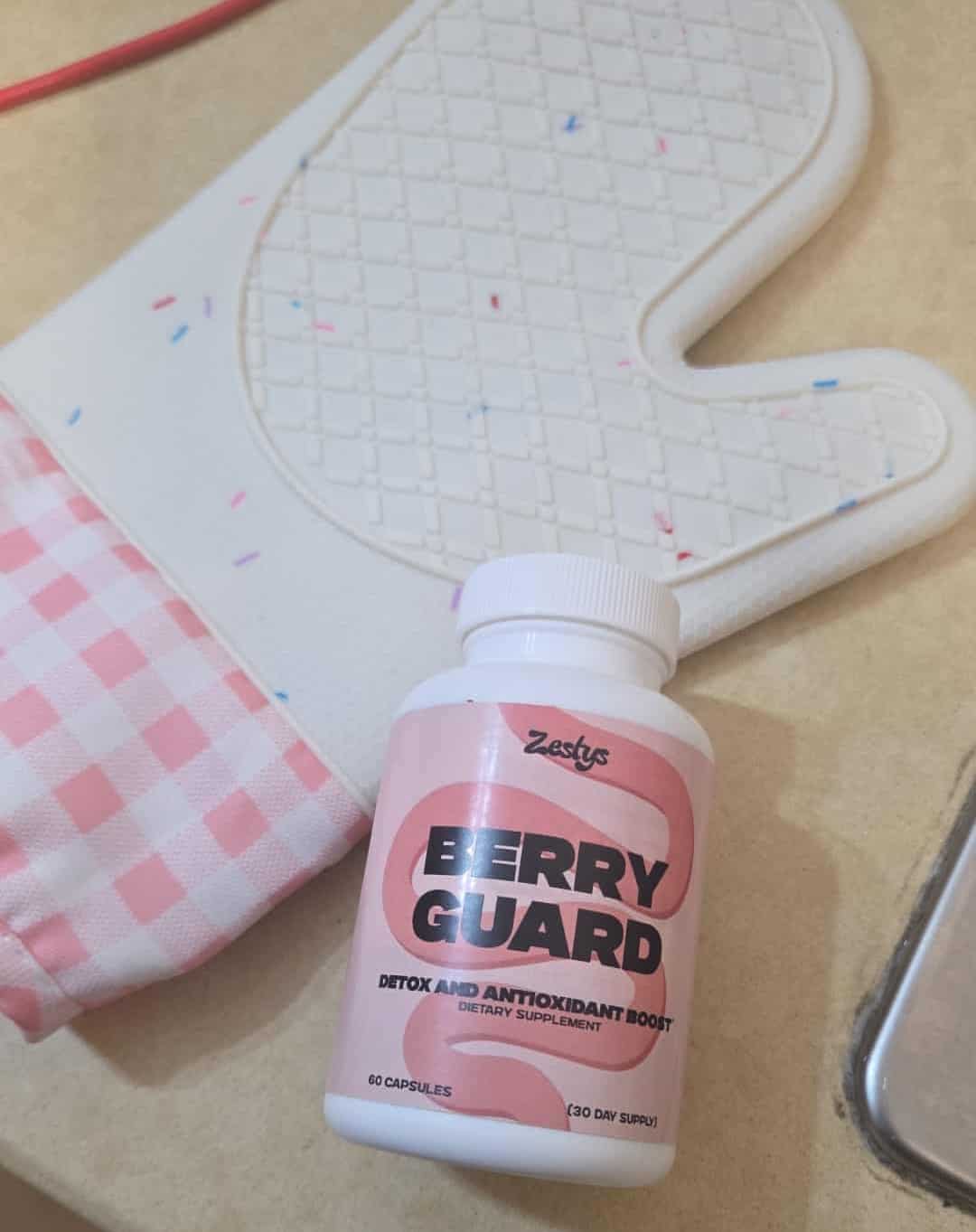 Berry Guard supplement bottle on a table with a pink checkered cloth and white heart-shaped object in the background.