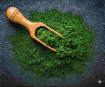 Wooden scoop in a pile of green powder on a dark surface