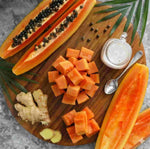 Sliced papaya on a wooden board with ginger and a small bowl of salt.