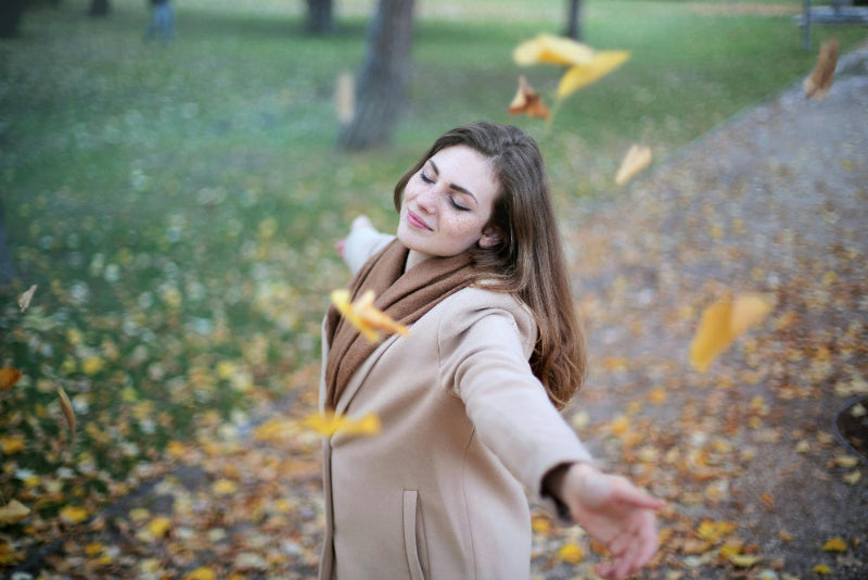 Woman in a beige coat standing in a park with falling leaves